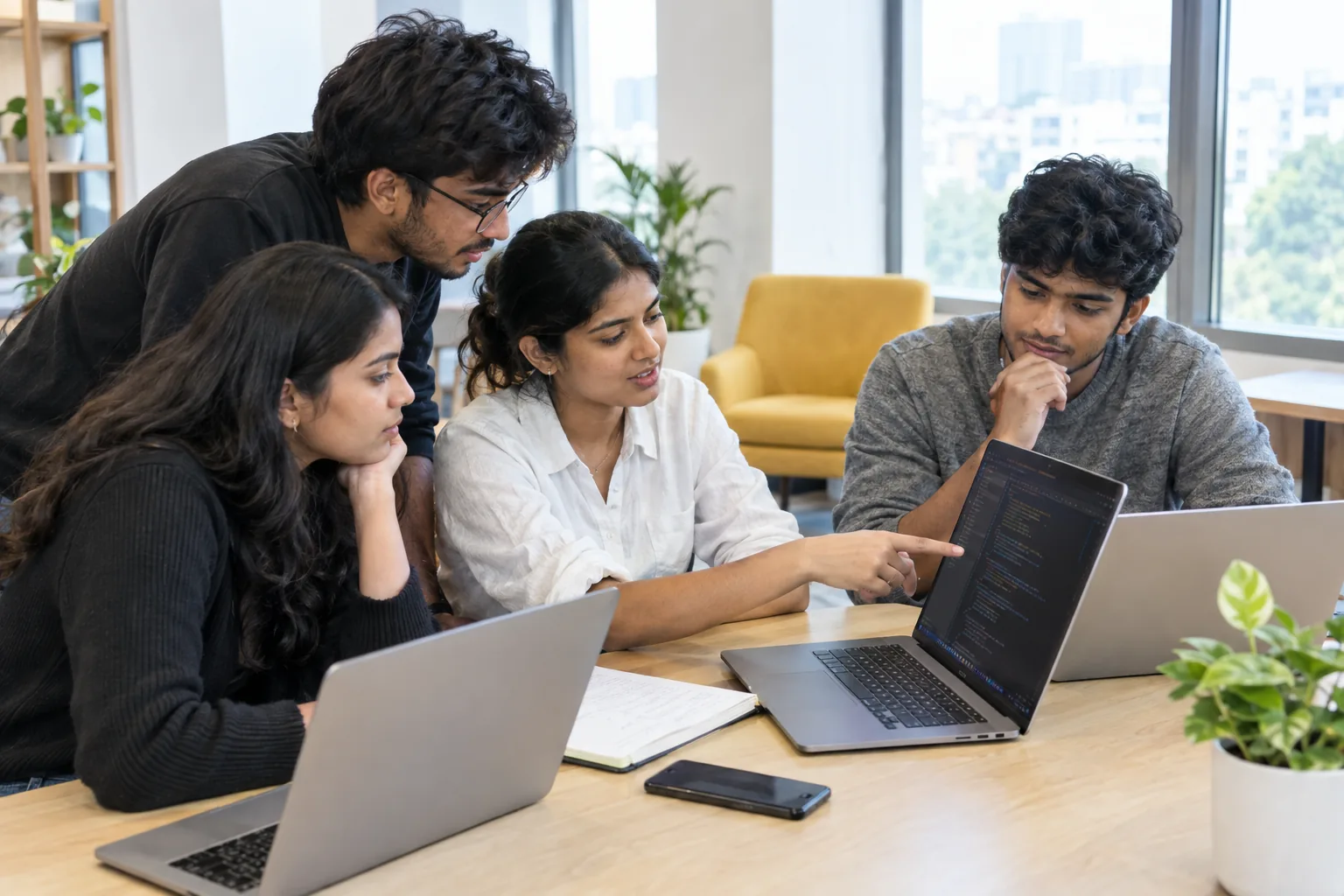Young developers collaborating around laptops in a modern Indian tech office